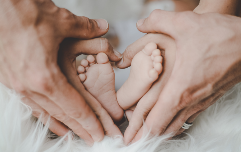 Couple's hands surrounding a baby's feet.